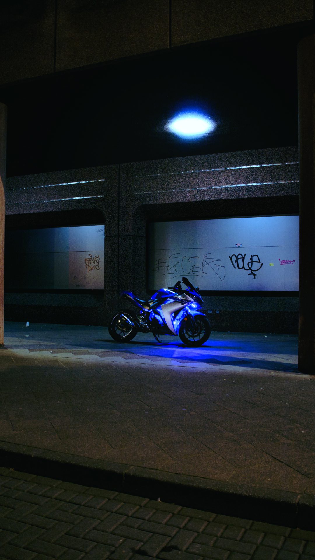 Motorrad bei Nacht mit blauem Licht vor urbaner Architektur.